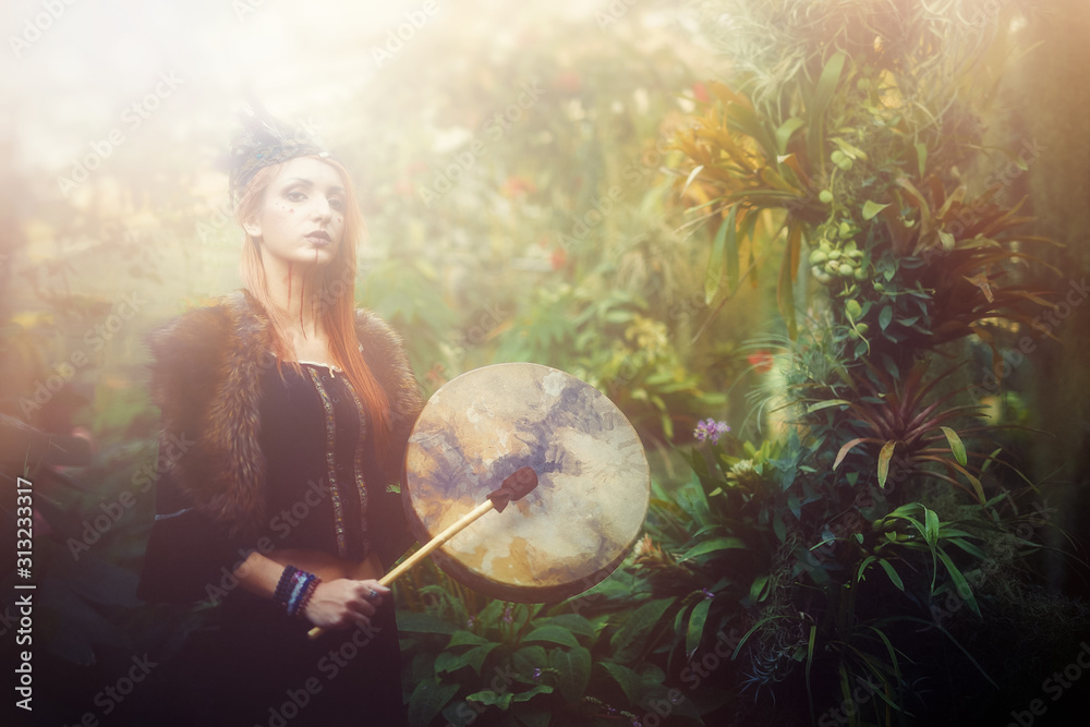 Naklejka premium beautiful shamanic girl playing on shaman frame drum in the nature.