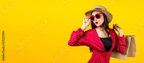 Banner of trendy shopaholic woman excited about new purchases or sales holding shopping bags and looking to side copy space over yellow background. Happy beautiful Asian woman carrying shopping bags.