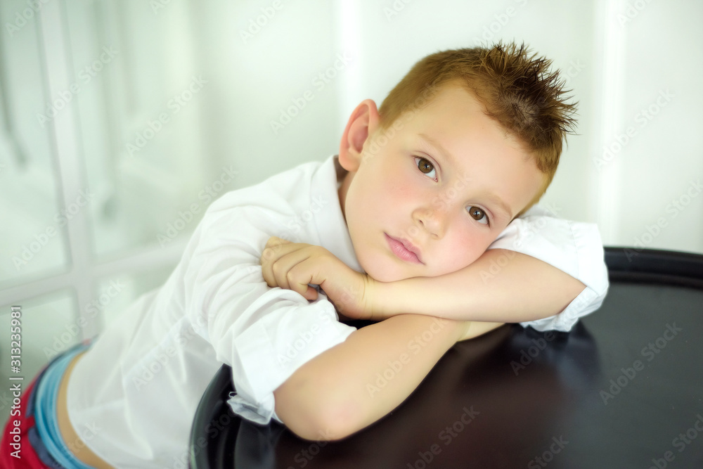 Portrait of 7 years old caucasian boy in white shirt with his hands near face. Fashionable good looking little boy looking in camera. Stylish trendy schoolboy in light room. Portrait of 7 years old caucasian boy in white shirt with his hands near face. Fashionable good looking little boy looking in camera. Stylish trendy schoolboy in light room.