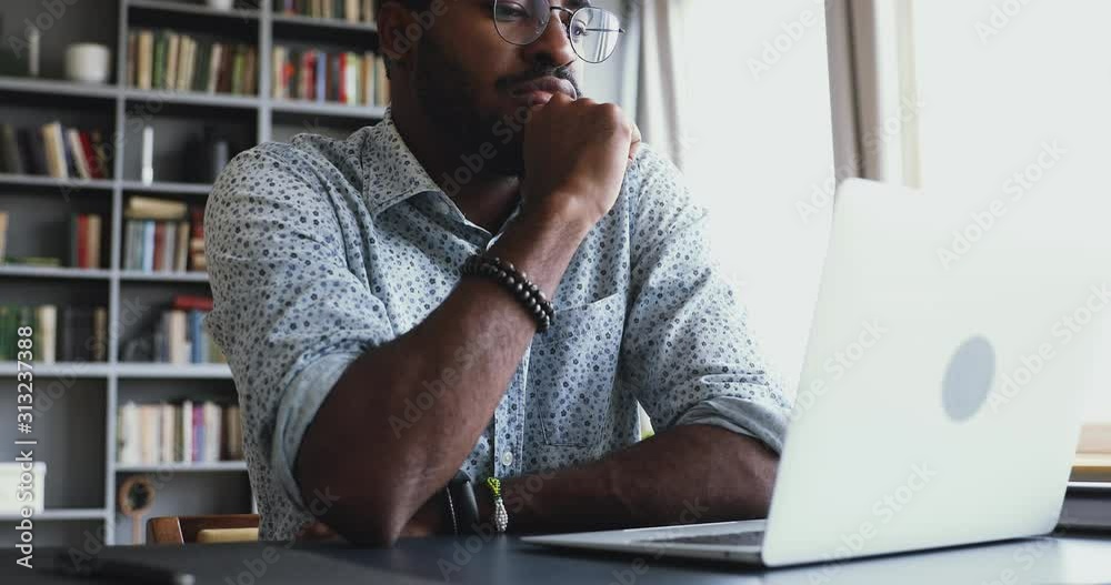 Serious thoughtful american businessman sit at desk look at laptop