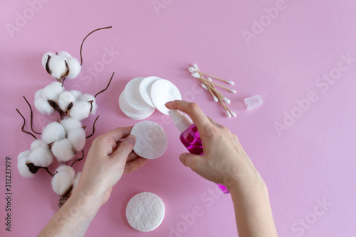 Cotton pads for removal makeup with woman hands and cosmetics on pink background flat lay.