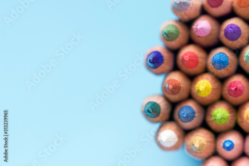Colored wooden artistic graphite pencils tips in close-up background. Colored sharp pencil leads of multi-colored pencils in macro on a light blue background with copy space.