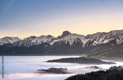 swiss mountain range in switzerland while the valley is covered in fog during sunset, super warm light and clear sky