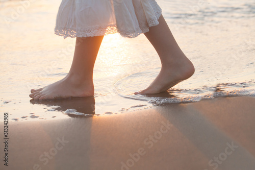 Beautiful woman legs on the beach with sea surf at sunset