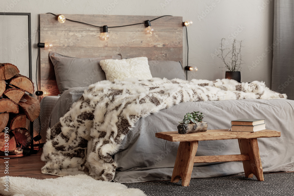 Wooden bench in the foot of the bed with grey bedding and cozy blanket - obrazy, fototapety, plakaty 