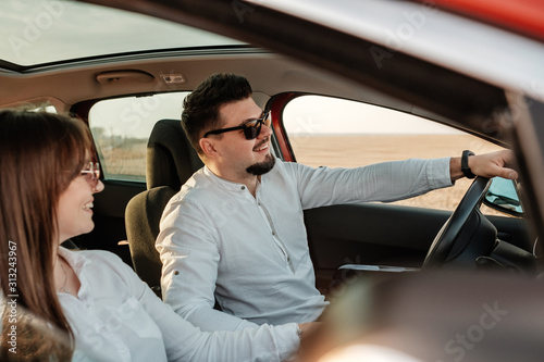 Young Happy Couple Dressed Alike in White Shirt and Jeans Enjoying Road Trip at Their New Car, Beautiful Sunset on the Field, Vacation and Travel Concept © Romvy