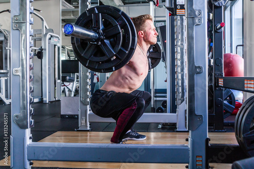 Caucasian man performing barbell squats at the indoor gym.