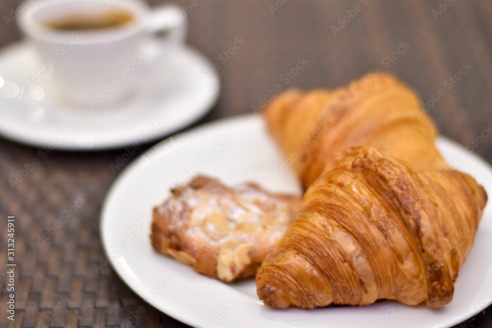 Croissant bread in a white plate on a wooden table with coffee.