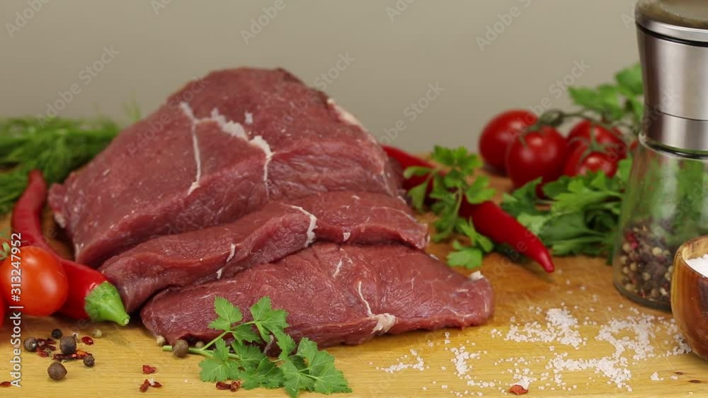 Beef steaks and vegetables on a wooden board on a gray background, close-up Beef steaks and vegetables on a wooden board on a gray background, close-up