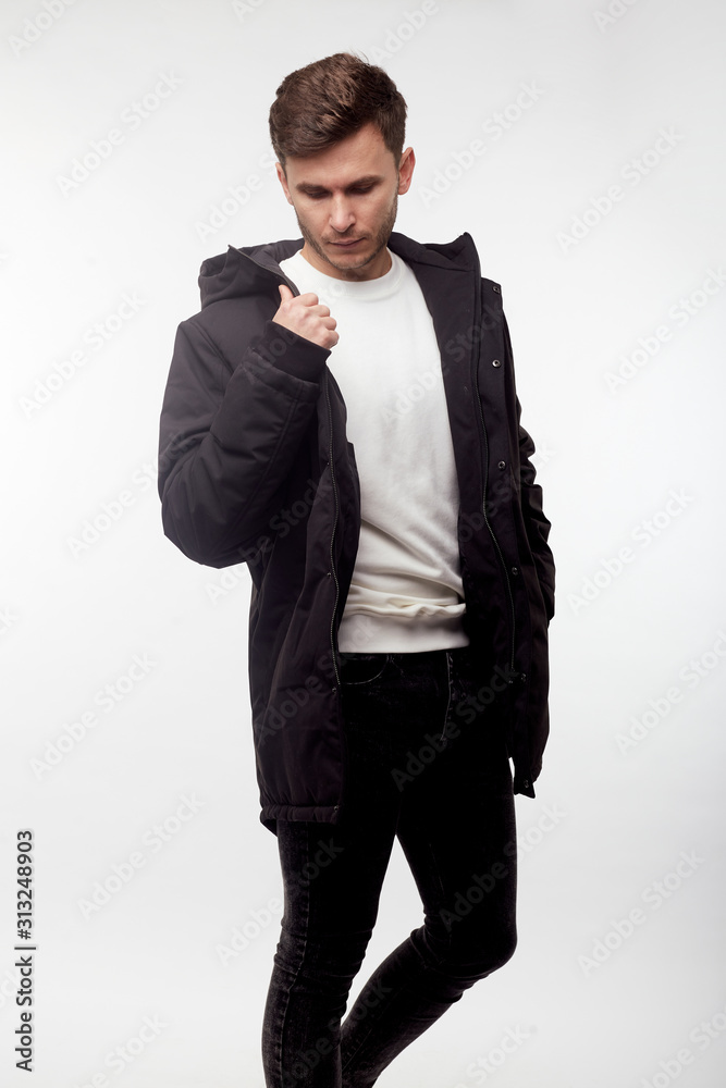 Young european man in white sweater and black pants, black down jacket posing on white background. Isolated. Young european man in white sweater and black pants, black down jacket posing on white background. Isolated.