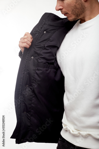 Young european man in white sweater and black pants, black down jacket posing on white background. Isolated.