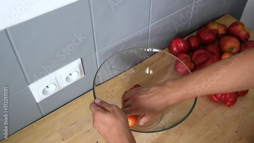 Close up of male hands putting red fresh tomatoes into a glass bowl photo