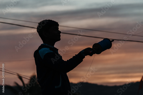 Silhouette of an Indian kid holding kite in his hands during the sunset at Makar Sankrati Festival in Wankaner, Gujarat, India