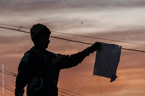 Silhouette of an Indian kid holding kite in his hands during the sunset at Makar Sankrati Festival in Wankaner, Gujarat, India
