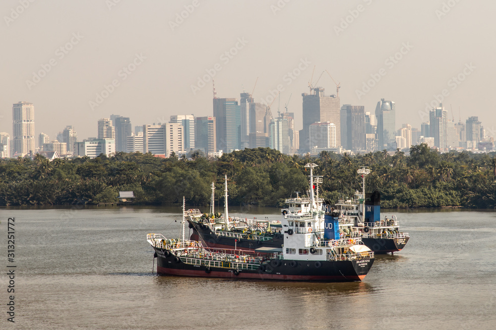 Two cargo ship parked in the middle of the river and in front of a green tree by the Chao Phraya River.