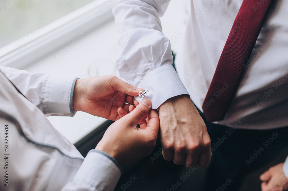A man, a friend helps fasten the sleeves and cufflink to the groom. Hands of two men close-up. Morning and preparation of the groom. Wedding, holiday, photography. A man, a friend helps fasten the sleeves and cufflink to the groom. Hands of two men close-up. Morning and preparation of the groom. Wedding, holiday, photography.