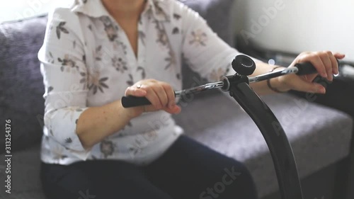 Senior woman doing exercises at home for wrist at a medical device, kinetotherapy device