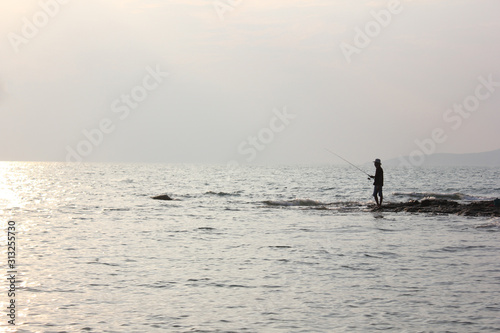 Silhouette of man fishing on the beach at sunset.