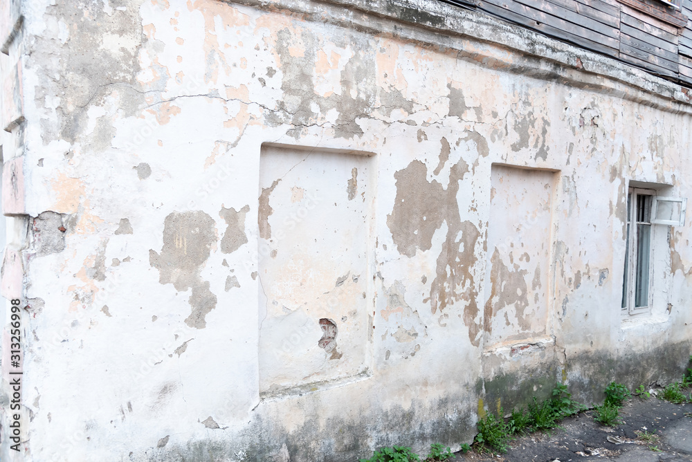 Fragment of the wall of the old building facade, peeling white paint, under which a cement texture.