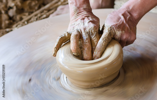 Hands of a potter make a vessel of clay on a pottery wheel.