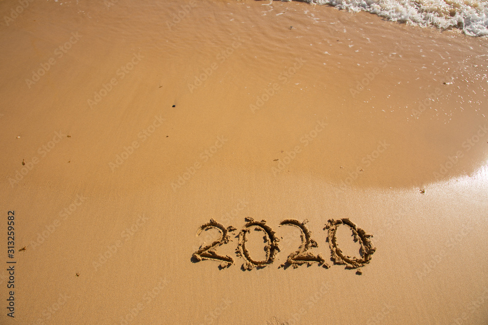Fototapeta premium Summer beach holiday 2020 season golden sand - year - decade - new season lettering on the beach with wave and clear blue sea. Numbers 2020 year on the sea shore, message handwritten New Years concept