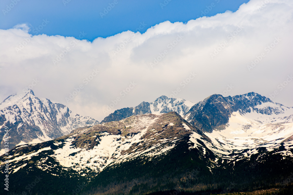 high tatras mountain ridge in springtime. snow capped rocky peaks in dramatic dappled sunlight beneath a clouds on a blue sky. place where earth meets sky concept