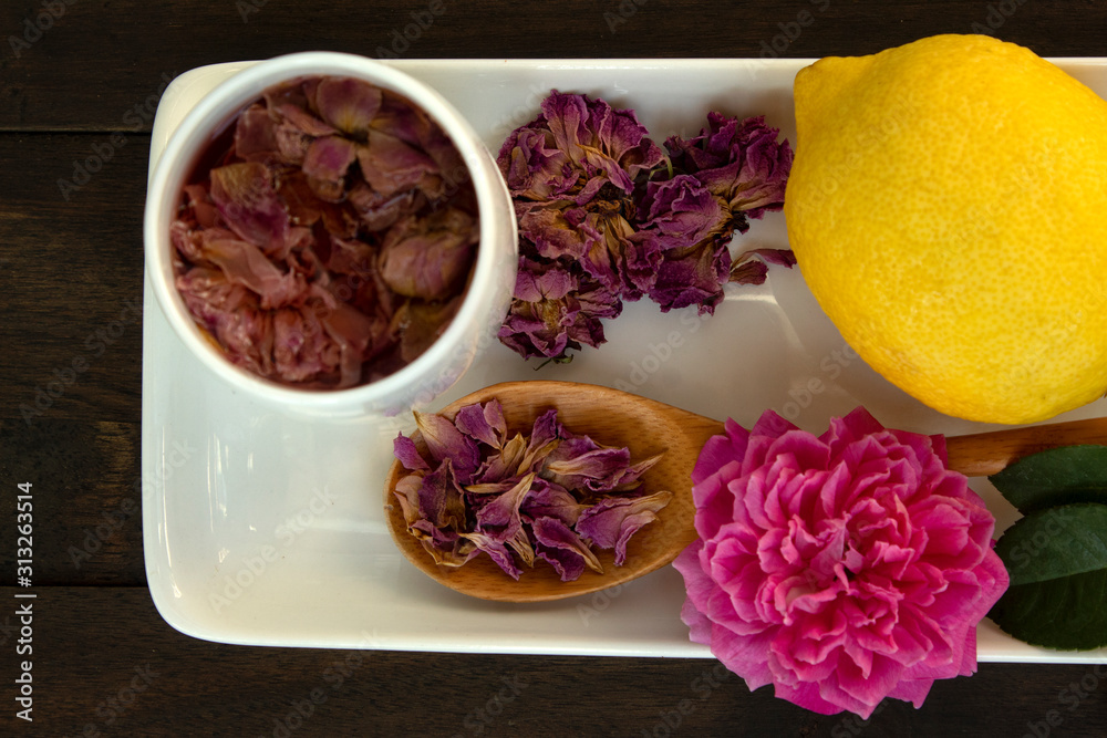 dried pink roses and tea in glass on black wood background, dry rose petala in wood spoon