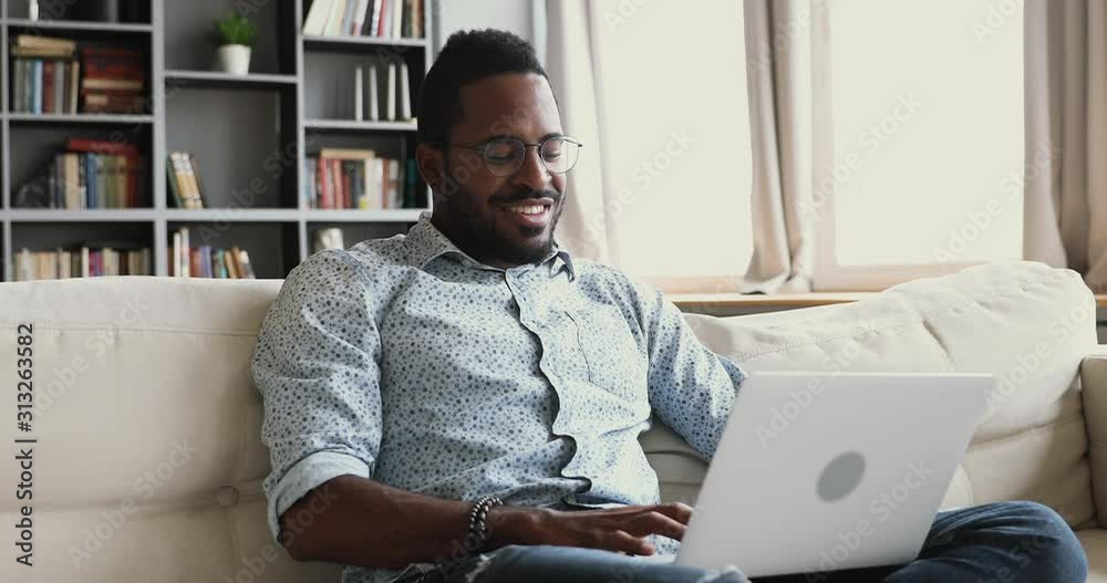 Happy african man using laptop surfing internet sit on sofa
