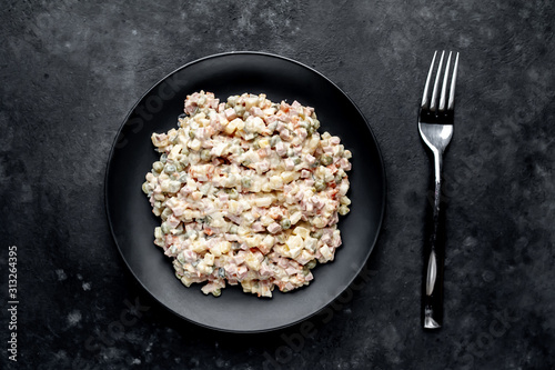 Olivier salad on a black plate on a stone background with copy space for your text, traditional Russian dish