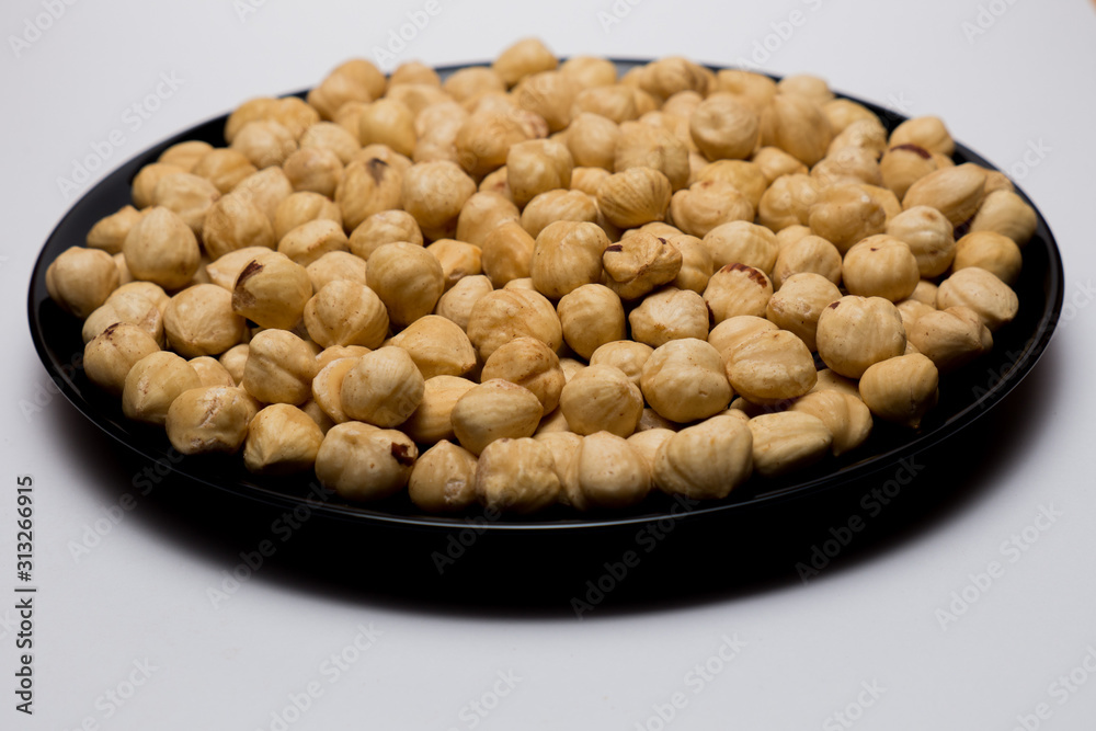 Whole hazelnuts in black plate on the white background. Healthy vegetarian snack. Close-up photo. Vegetable diet. Whole hazelnuts in black plate on the white background. Healthy vegetarian snack. Close-up photo. Vegetable diet.