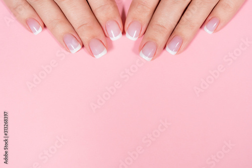 Closeup top view of two beautiful female hands with elegant professional fresh french pink and white manicure isolated on pastel pink background. Horizontal color flatlay photography with copyspace.