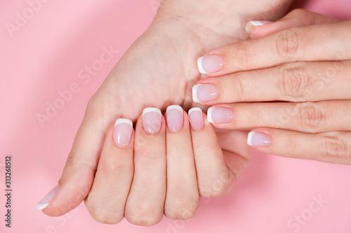 Closeup top view of two beautiful female hands with classic white and pink french manicure at fingernails. Hands isolated on pastel pink background. Horizontal flatlay color photography.
