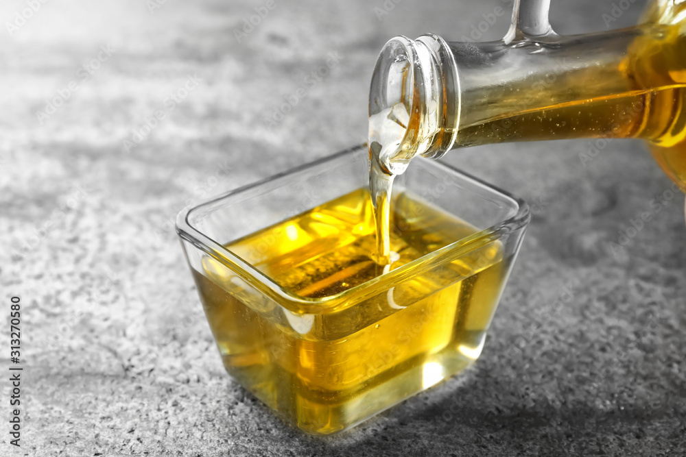 Pouring cooking oil from jug into bowl on grey table Pouring cooking oil from jug into bowl on grey table