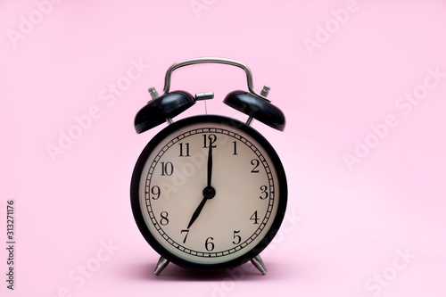 Black retro alarm clock on a pink background. The hands of the clock stand at 7 am. The beginning of the day. Minimalism