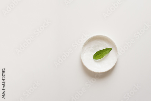 Means for skin care, rejuvenation and hydration of the face. Cream, moisturizing lotion on a white background with a green leaf. The concept of self-care and care for the skin