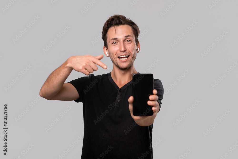 Young handsome man with wireless earbuds pointing at the screen of a smartphone. Young handsome man with wireless earbuds pointing at the screen of a smartphone.
