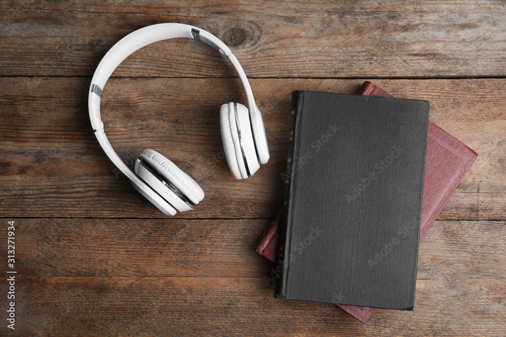Book and modern headphones on wooden table, flat lay Book and modern headphones on wooden table, flat lay