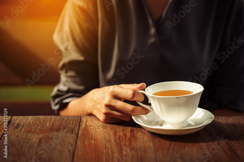 Woman s hands holding white cup of tea or coffee on sun light. Morning time for breakfast