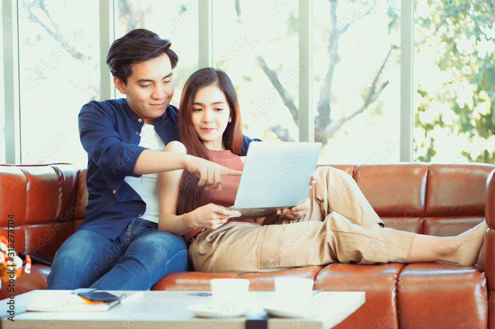Excited young couple looking at laptop. Young couple watching media content online in a tablet sitting on a sofa in the living room. Excited young couple looking at laptop. Young couple watching media content online in a tablet sitting on a sofa in the living room.