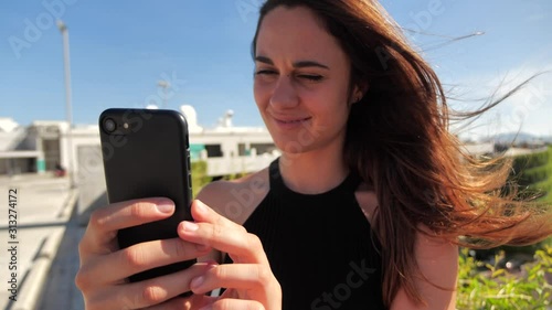 close-up portrait of smiling young elegant bissneswoman lwith deep brown eyes in black dress trying to buy something enjoyable with her smartphone Urban city background. Slow motion 4k photo