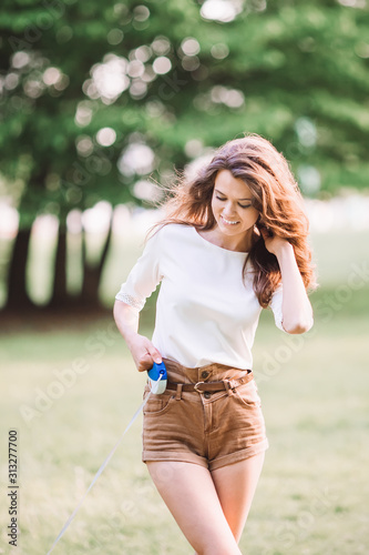 Beautiful girl walking in the park with a small dog and smiling