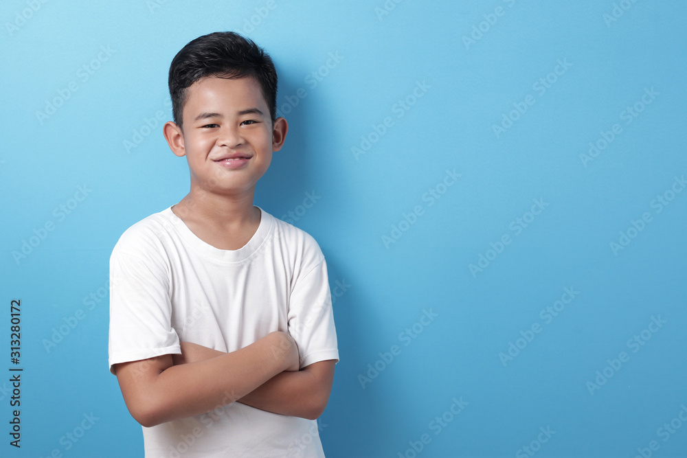 Asian boy looks at the camera and smiles happily, crosses his arms in front of his chest