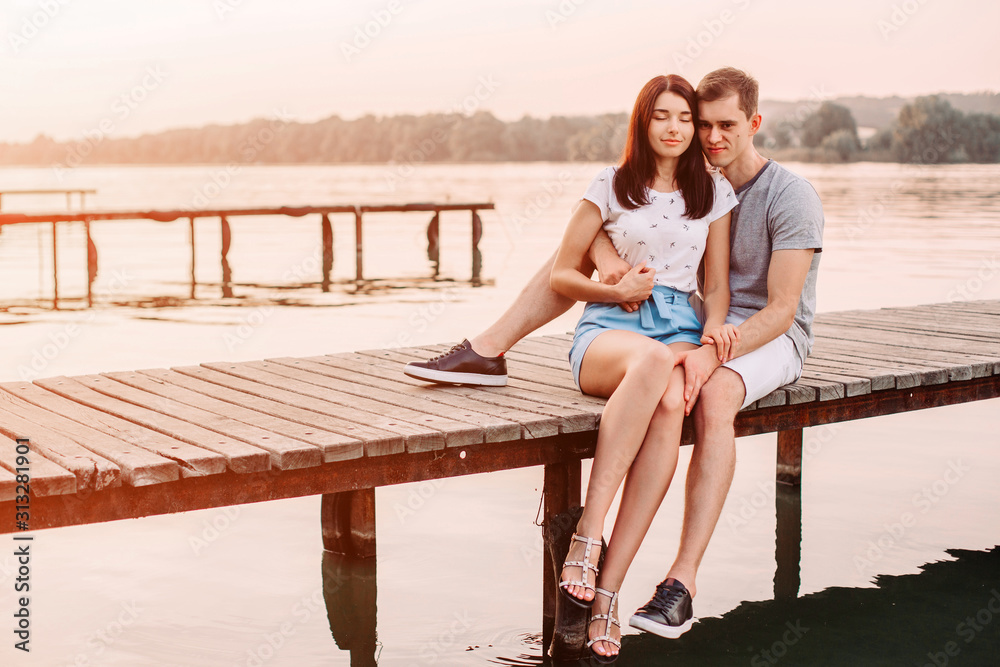 Loving young couple hugging on pier at sunset in summer.