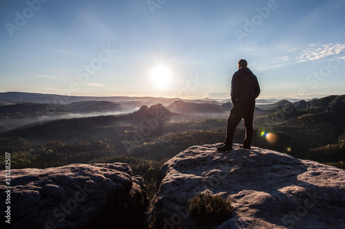 rear view of a young man standing on the top of a rock watching the sunrise above the forest photo