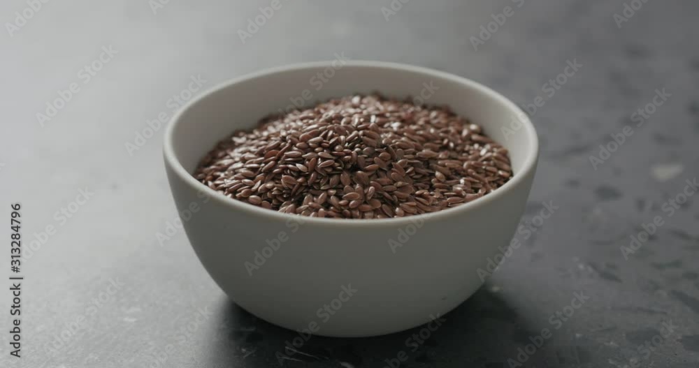 Slow motion handheld shot of flaxseed in white bowl on terrazzo countertop Slow motion handheld shot of flaxseed in white bowl on terrazzo countertop