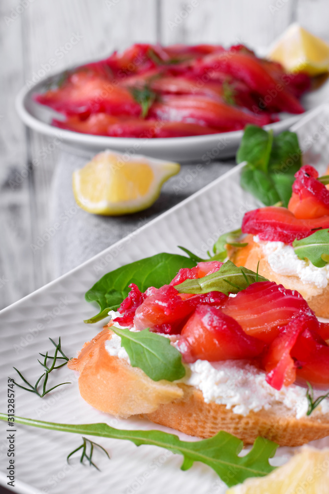 Trout Gravlax on the slices of white bread with ricotta topped with greenery against the white background. Nordic cuisine meal