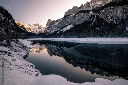 winter view of lake Gosau with fresh snow on majestic mountains, forest and reflection on the lake