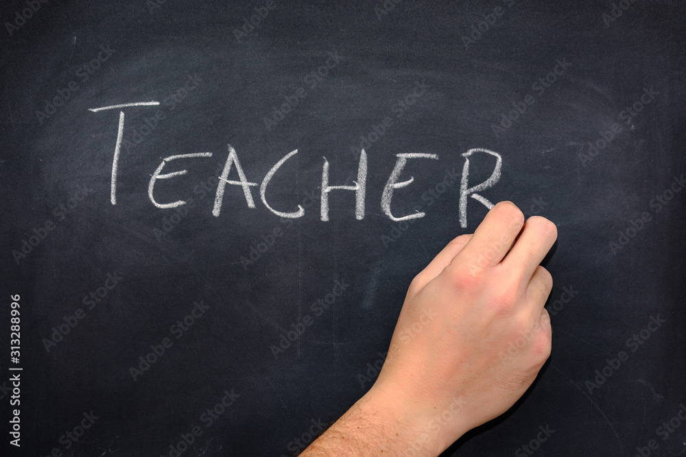 Teacher's hand writing the word teacher on a blackboard Teacher's hand writing the word teacher on a blackboard