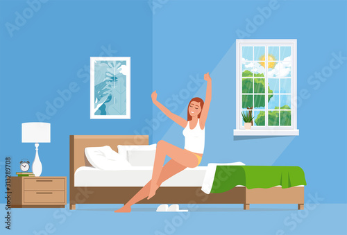 The girl wakes up and stretches out sitting on the bed smiling in the morning.