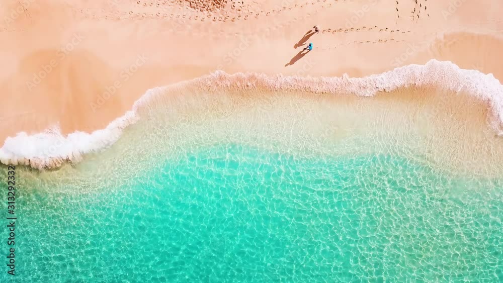 Couple walk along the perfect tropical beach with calm rolling waves